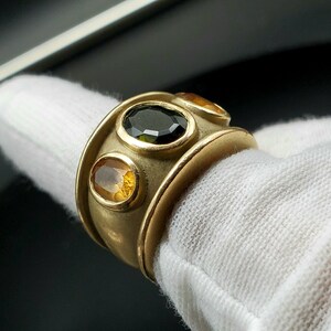 May include: A gold ring featuring three oval-shaped gemstones. The central stone is black, and the two outer stones are yellow.