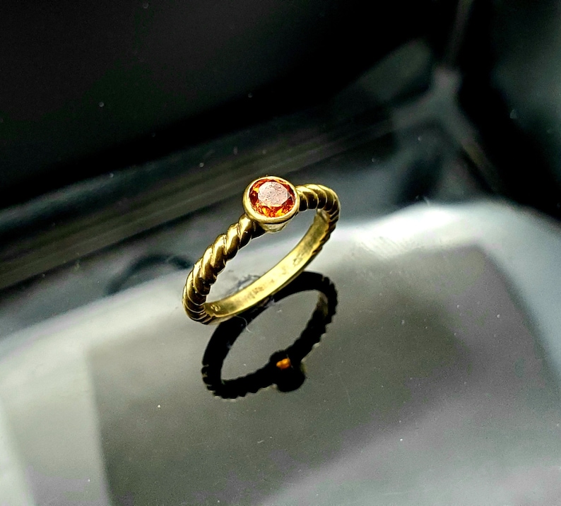 May include: A gold ring with a twisted band and a small, round, orange gemstone.