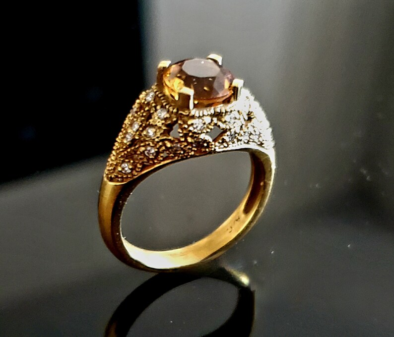 May include: A gold ring with a large, oval-shaped brown gemstone surrounded by smaller, white gemstones. The ring has a delicate, intricate design.