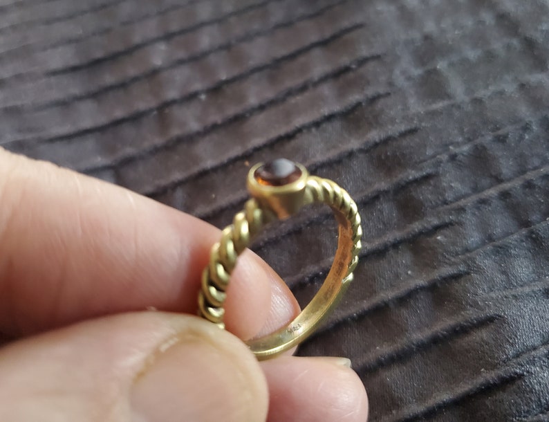 May include: A gold ring with a brown gemstone set in a twisted band.