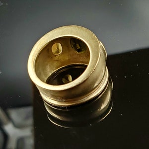 May include: A gold ring with three round gemstones set into the band. The ring is thick and has a wide band.