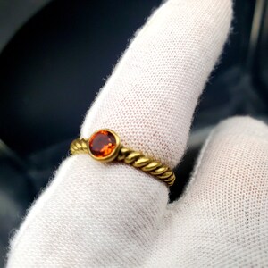 May include: A gold ring with a twisted band and a round orange gemstone.