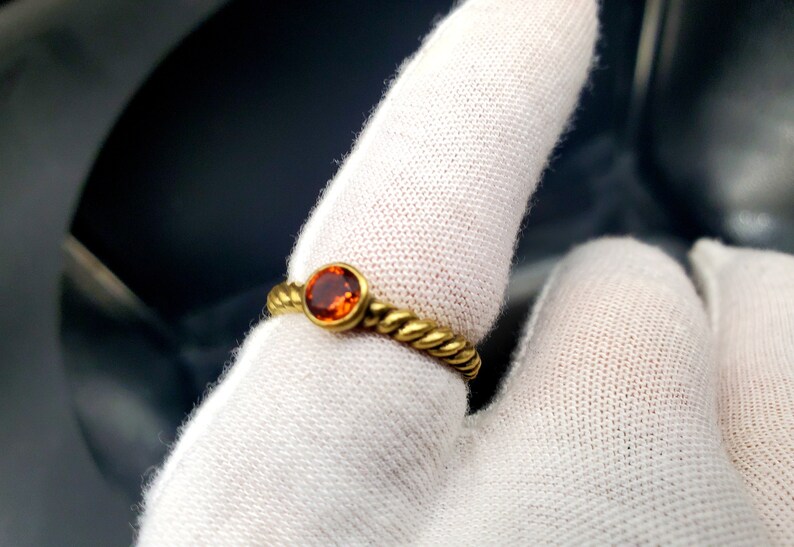 May include: A gold ring with a twisted band and a round orange gemstone.