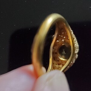 May include: A gold ring with a large, round, clear stone surrounded by smaller stones. The ring is set in a simple band.