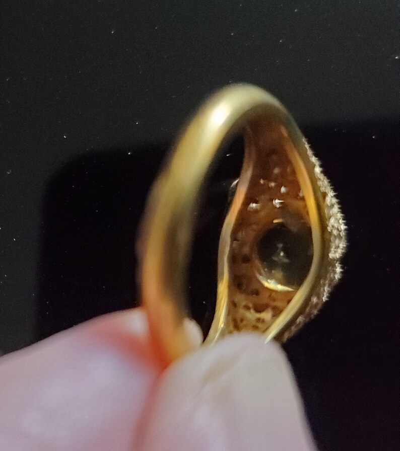 May include: A gold ring with a large, round, clear stone surrounded by smaller stones. The ring is set in a simple band.