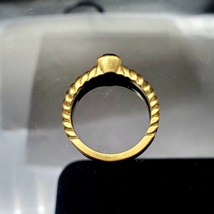May include: A gold ring with a twisted band design. The ring is simple and elegant.