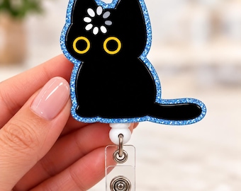 Könnte beinhalten: Ein Ausweishalter in Form einer schwarzen Katze mit blauem Glitzerrand. Die Katze hat große gelbe Augen und ein weißes Ladesymbol auf der Stirn. Der Ausweishalter verfügt über ein transparentes Kunststoffband mit einem Metalldruckknopf.