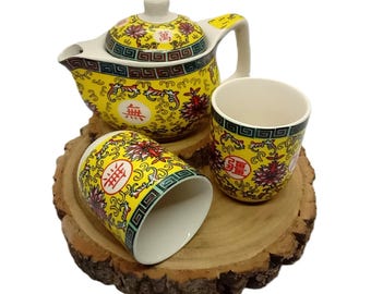 May include: A yellow and red Chinese tea set with a teapot and two cups. The set is decorated with floral patterns and Chinese characters. The set is on a wooden base.