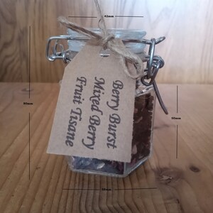 May include: A glass jar with a metal clasp lid filled with dried fruit and herbs. The jar is labelled "Berry Burst Mixed Berry Fruit Tisane". The jar is 50mm wide and 58mm tall.