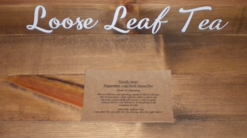 May include: A brown paper card with the text "Totally Mint Peppermint Leaf Herb Tea" and "Fresh & Cleansing" printed on it. The card is on a wooden surface with the text "Loose Leaf Tea" printed on the surface.
