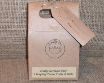 May include: A brown paper bag with a handle and a gift tag. The bag has a logo that says "Totally Tea" and a picture of a teapot. The bag says "Totally Tea Taster Pack, 6 Tempting Tisanes Fruits & Herbs".