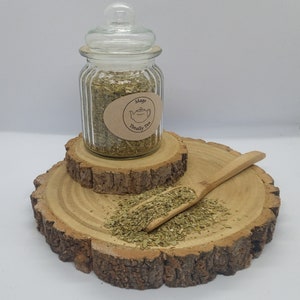 May include: A glass jar filled with dried green herbs, labelled "Mages Totally Tea", sitting on a wooden platform.