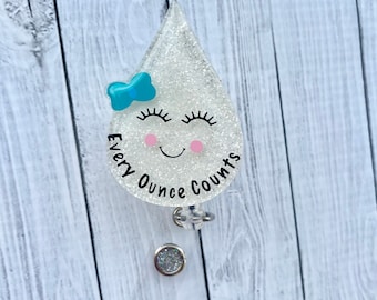 May include: A white glitter raindrop shaped badge holder with a blue bow, eyelashes, and pink cheeks. The text "Every Ounce Counts" is written on the raindrop.