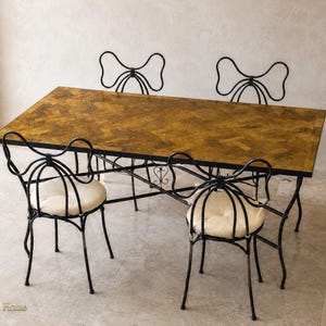 Peut inclure: Une table à manger rectangulaire avec un plateau en bois à motif chevrons marron et un cadre en métal noir, accompagnée de quatre chaises en métal noir avec des dossiers en forme de nœud et des coussins d'assise ronds blanc cassé.