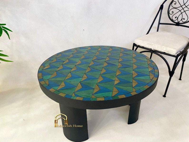 May include: A round mosaic coffee table with a geometric pattern of blue, green, and gold tiles. The table has a black base with three legs.
