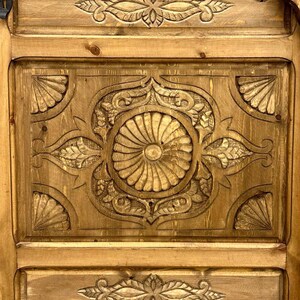 May include: A wooden door with intricate carvings in a light brown color. The carvings are in a floral pattern and are centered on the door.