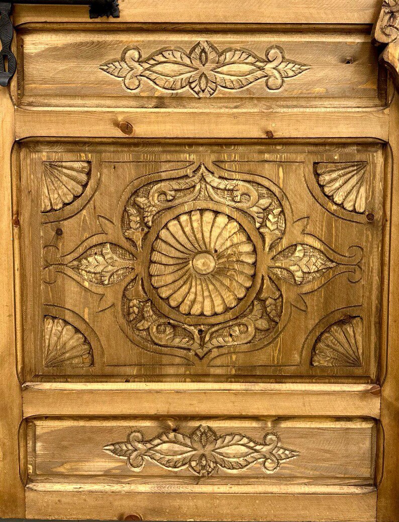 May include: A wooden door with intricate carvings in a light brown color. The carvings are in a floral pattern and are centered on the door.