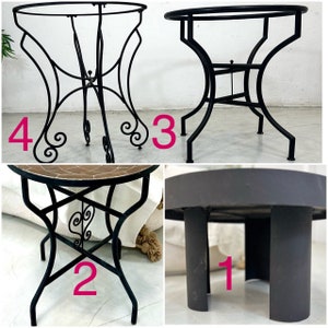 May include: Four black metal tables with different designs. The table on the top left has a round top and a decorative base. The table on the top right has a round top and a simple base. The table on the bottom left has a round top and a decorative base with a tile top. The table on the bottom right has a round top and a simple base.