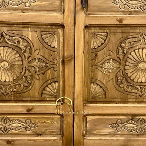 May include: A pair of wooden doors with intricate carved designs. The doors are a light brown color and have a brass handle.