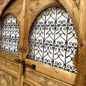 May include: A pair of intricately carved wooden doors with arched tops and decorative iron grilles. The doors are a rich brown color and feature intricate floral and geometric designs.
