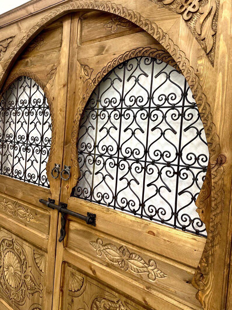 May include: A pair of intricately carved wooden doors with arched tops and decorative iron grilles. The doors are a rich brown color and feature intricate floral and geometric designs.