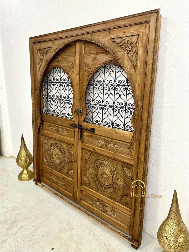 May include: A pair of intricately carved wooden doors with arched tops and metal grilles. The doors are a rich brown color and have a rustic, antique look. The doors are framed by a wooden surround.
