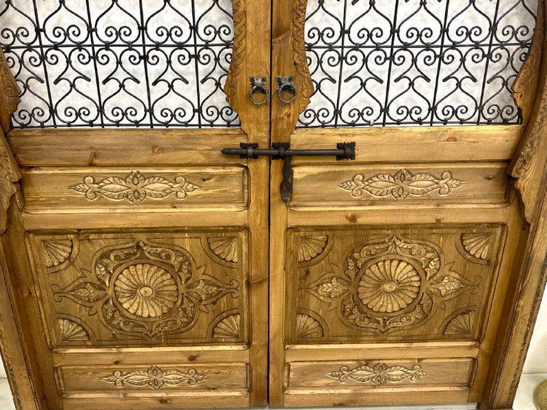 May include: A pair of wooden doors with intricate carved details and a metal latch. The doors have a decorative iron grate design at the top.
