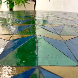 May include: A close-up of a mosaic table top with a geometric pattern of green, blue, and brown triangles.