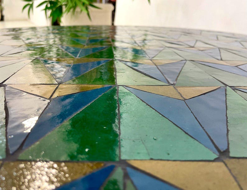 May include: A close-up of a mosaic table top with a geometric pattern of green, blue, and brown triangles.