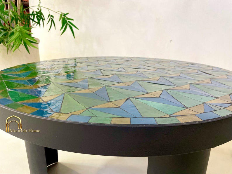 May include: A round mosaic table with a black base and a top made of green, blue, and beige tiles. The table is made of geometric shapes and has a glossy finish.