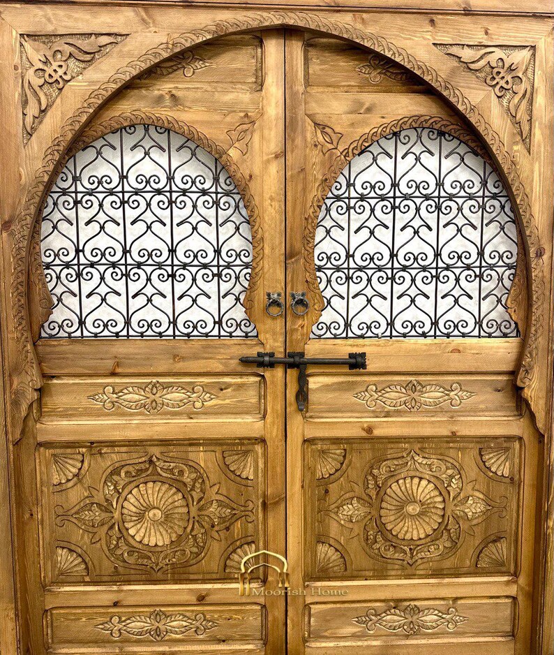May include: A pair of intricately carved wooden doors with arched tops and metal latticework panels. The doors are painted in a warm brown color and feature decorative floral motifs.