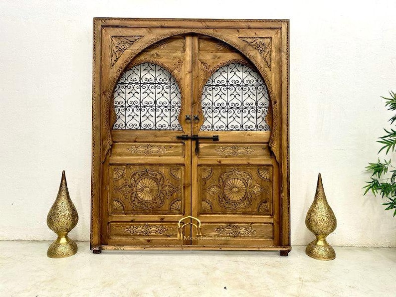 May include: A wooden double door with intricate carvings and a metal lattice design. The door is painted a dark brown color and has a traditional Moroccan style.