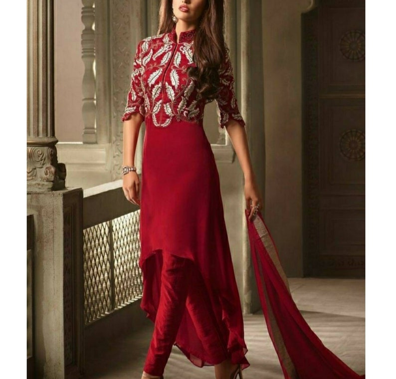 May include: A red dress with a high neck and a white embroidered design. The dress has a high-low hemline and is paired with red pants.