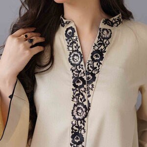 May include: Cream-colored tunic with black floral embroidery along the neckline. The long-sleeved top has a V-neck design and a relaxed fit. The sleeves have a flared design with black trim.