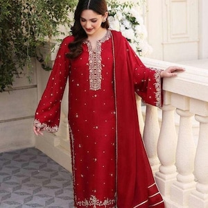 K&ouml;nnte beinhalten: Ein rotes, lang&auml;rmliges Kleid mit goldener Stickerei und einem passenden roten Dupatta mit goldenen Verzierungen.