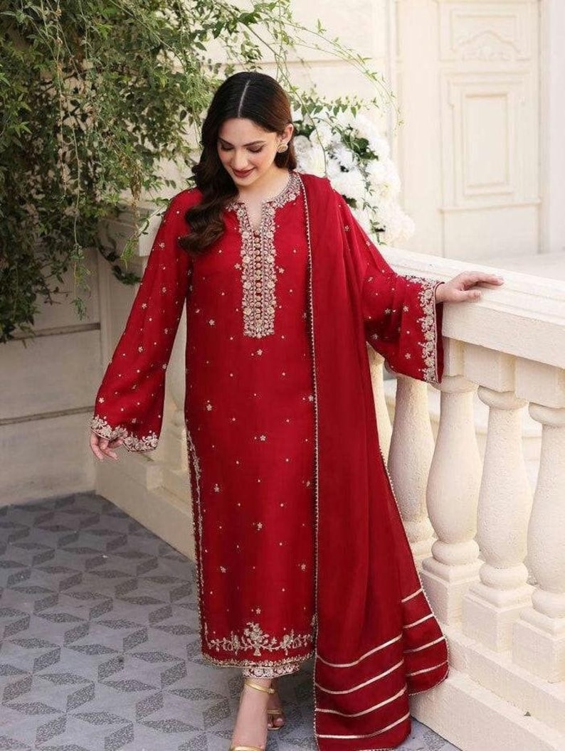 K&ouml;nnte beinhalten: Ein rotes, lang&auml;rmliges Kleid mit goldener Stickerei und einem passenden roten Dupatta mit goldenen Verzierungen.