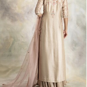 Pu&ograve; includere: Una lunga kurta beige con ricami floreali intricati e un dupatta abbinato. La kurta ha una scollatura rotonda e maniche a tre quarti. Il dupatta &egrave; trasparente e presenta un delicato motivo floreale.