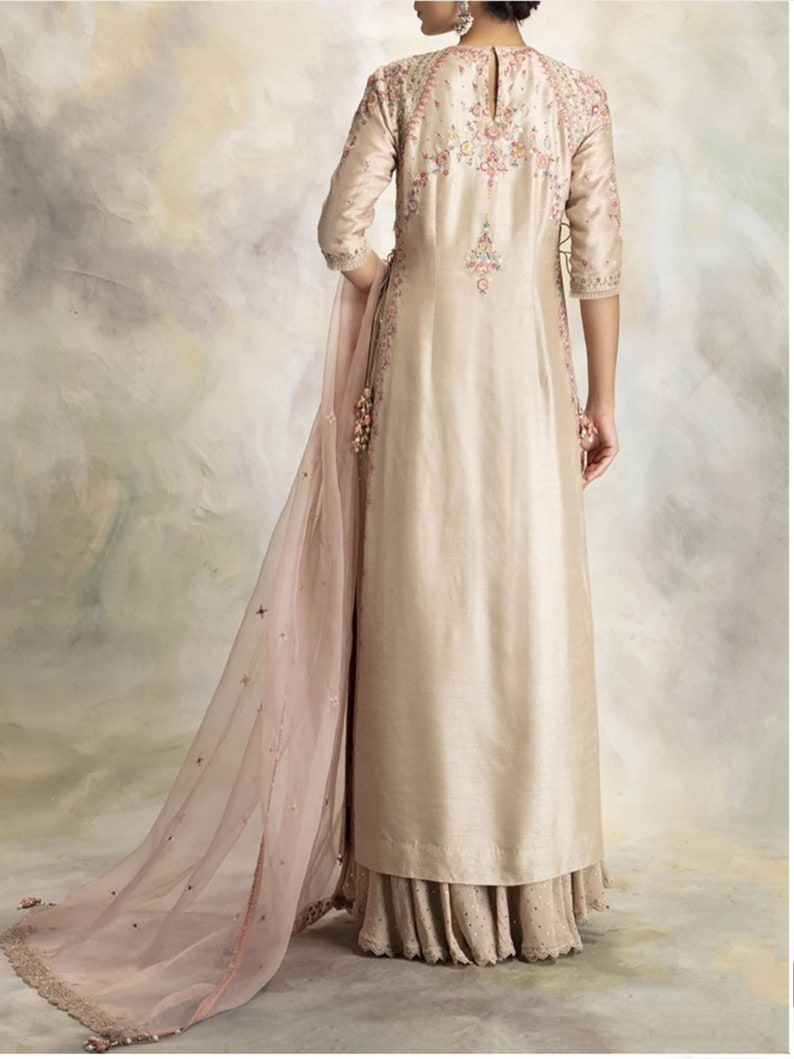 Pu&ograve; includere: Una lunga kurta beige con ricami floreali intricati e un dupatta abbinato. La kurta ha una scollatura rotonda e maniche a tre quarti. Il dupatta &egrave; trasparente e presenta un delicato motivo floreale.