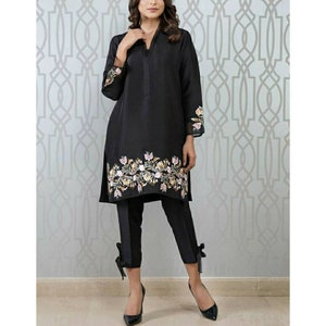 May include: A black long-sleeved tunic with a floral embroidered hemline. The tunic is paired with black pants that have a bow detail at the ankles.