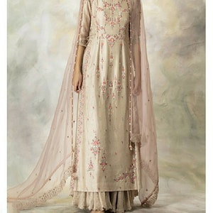 Pu&ograve; includere: Un lungo abito beige con ricami floreali e un dupatta rosa trasparente abbinato. L'abito ha una scollatura rotonda e maniche a tre quarti. Il dupatta ha un bordo in pizzo.