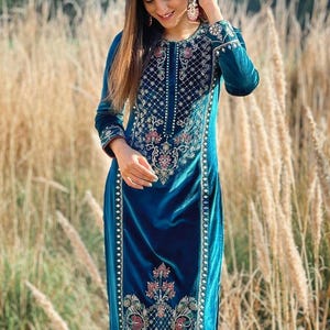 Puede incluir: Una kurta de terciopelo azul turquesa con intrincados bordados dorados y plateados. La kurta presenta un escote redondo y mangas largas. El bordado incluye motivos florales y geométricos.