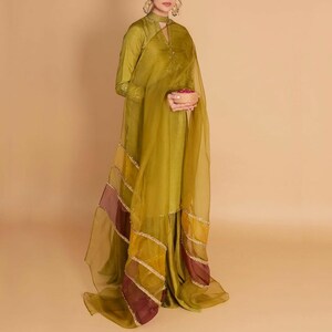 May include: A long green dress with a high neck and long sleeves. The dress has a sheer overlay with gold and burgundy accents. The dress is worn by a person holding a bowl of red berries.