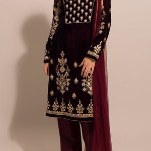 Puede incluir: Una kurta de terciopelo burdeos con bordados dorados y plateados. La kurta tiene un escote redondo y mangas largas. Se combina con pantalones burdeos a juego y una dupatta de red burdeos con bordados dorados.