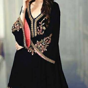 May include: Black tunic with ornate embroidery in gold, pink, and green. The tunic features a V-neck and flared sleeves with a scalloped hem. The sleeves have a pink lining. The garment is a stylish piece of clothing.