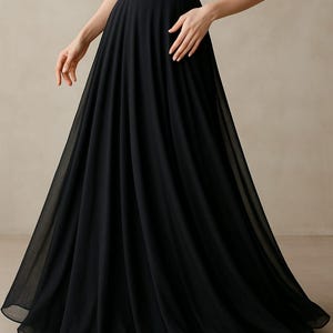 Könnte beinhalten: Ein schwarzes, bodenlanges Rock- und Top-Ensemble. Der Rock ist fließend und aus leichtem Stoff gefertigt, wodurch eine anmutige Silhouette entsteht. Das Oberteil ist ein schlichtes, ärmelloses Design. Das Outfit ist für formelle Anlässe geeignet.