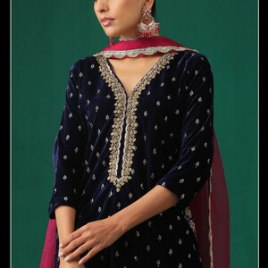 May include: A navy blue velvet kurta with gold embroidery and a pink dupatta. The kurta has a V-neckline and is adorned with small white dots.