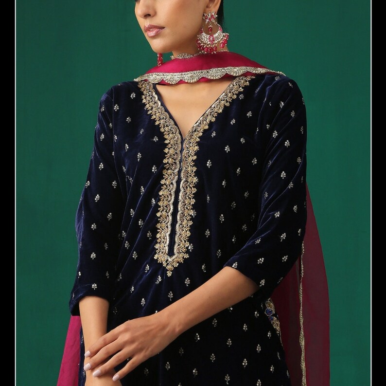 May include: A navy blue velvet kurta with gold embroidery and a pink dupatta. The kurta has a V-neckline and is adorned with small white dots.
