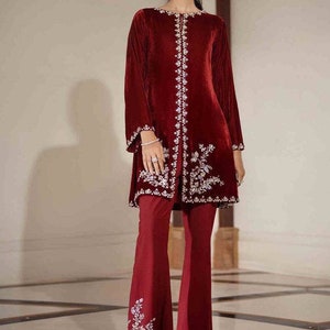 Puede incluir: Una blusa de terciopelo granate con bordados plateados y un pantalón granate a juego con bordados plateados en la parte inferior.