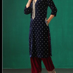 May include: A navy blue velvet kurta with gold embroidery and a maroon velvet salwar. The kurta has a V-neckline and three-quarter sleeves. The salwar has a wide leg and is embroidered at the hem.