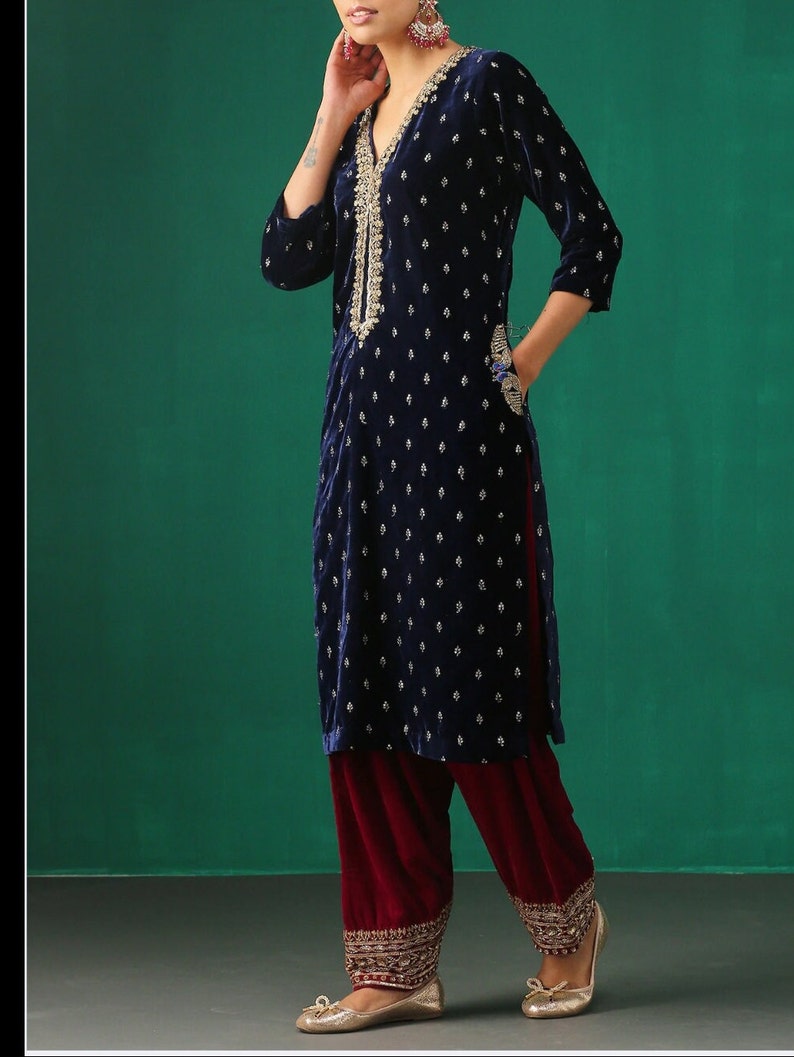 May include: A navy blue velvet kurta with gold embroidery and a maroon velvet salwar. The kurta has a V-neckline and three-quarter sleeves. The salwar has a wide leg and is embroidered at the hem.